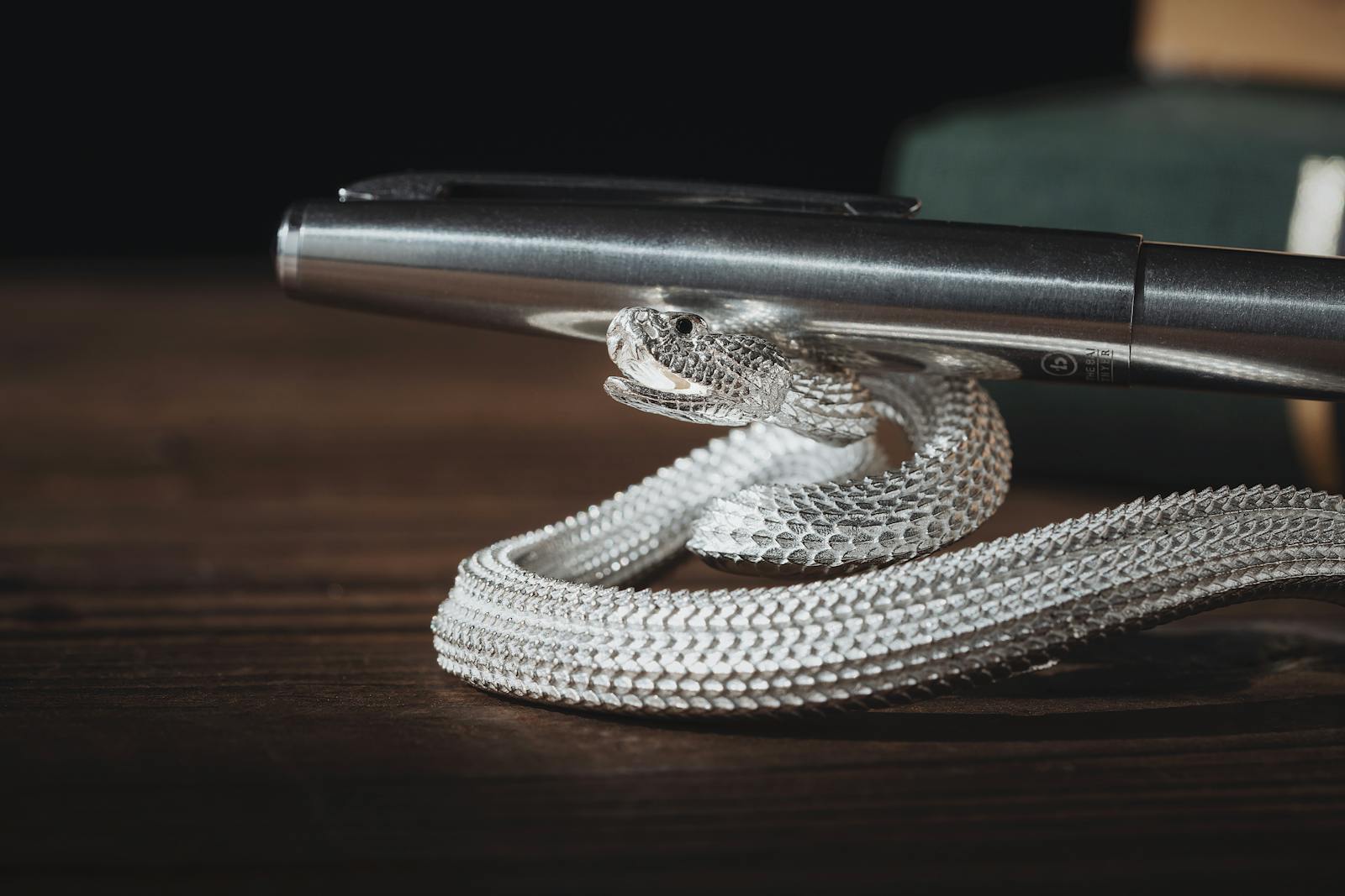 Close-up of a silver snake-shaped pen holder elegantly resting on a wooden surface with a metallic pen.